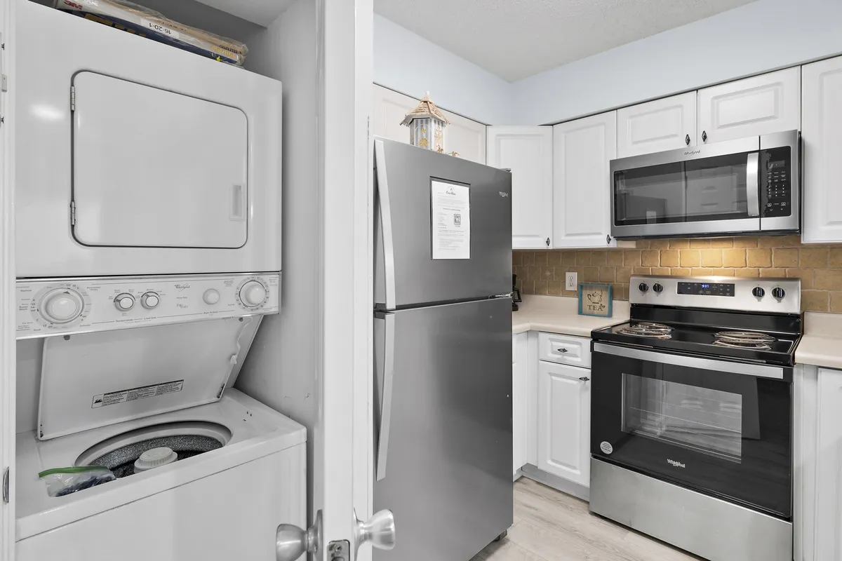 A practical, welcoming kitchen and laundry space featuring a stacked washer and dryer, stainless steel refrigerator, electric stove with oven, and microwave. The bright setting suggests convenience for meal prep and laundry, supporting extended stays and daily routines.