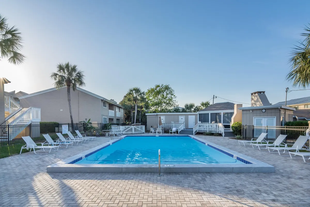 A spacious, palm-framed heated swimming pool surrounded by lounge chairs and cabana-style structures, set in a tranquil resort environment. The pool's inviting waters and relaxed lounging areas evoke a sense of leisurely, family-friendly outdoor enjoyment.