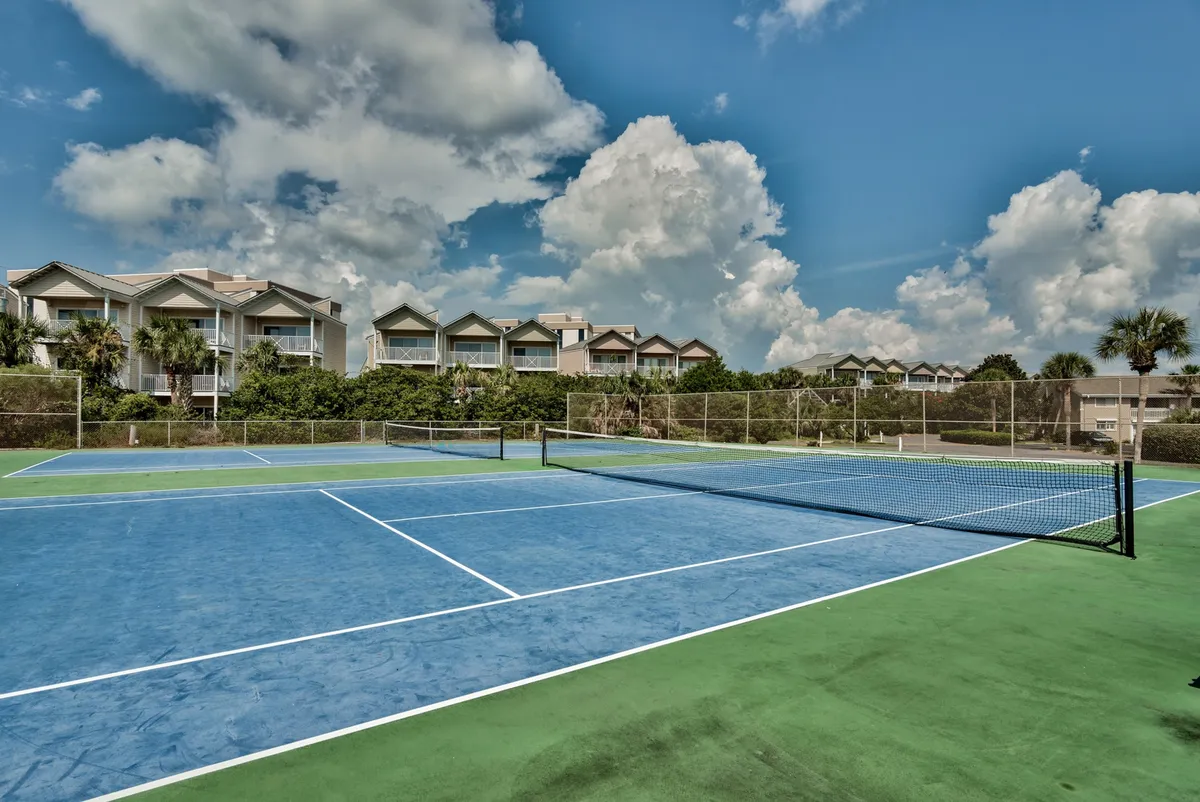 A dynamic view of tennis courts with blue and green surfaces, surrounded by lush greenery and the community’s condo buildings in the background. The courts are empty, emphasizing availability and inviting guests to enjoy active recreation.