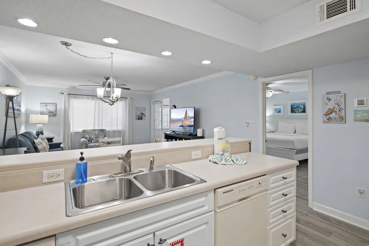 The open-plan living area flows from a welcoming kitchen into a cozy lounge space, complete with a comfortable couch, ambient lighting, and decor that feels like home. The television displays a scenic view, enhancing the sense of relaxation and leisure.