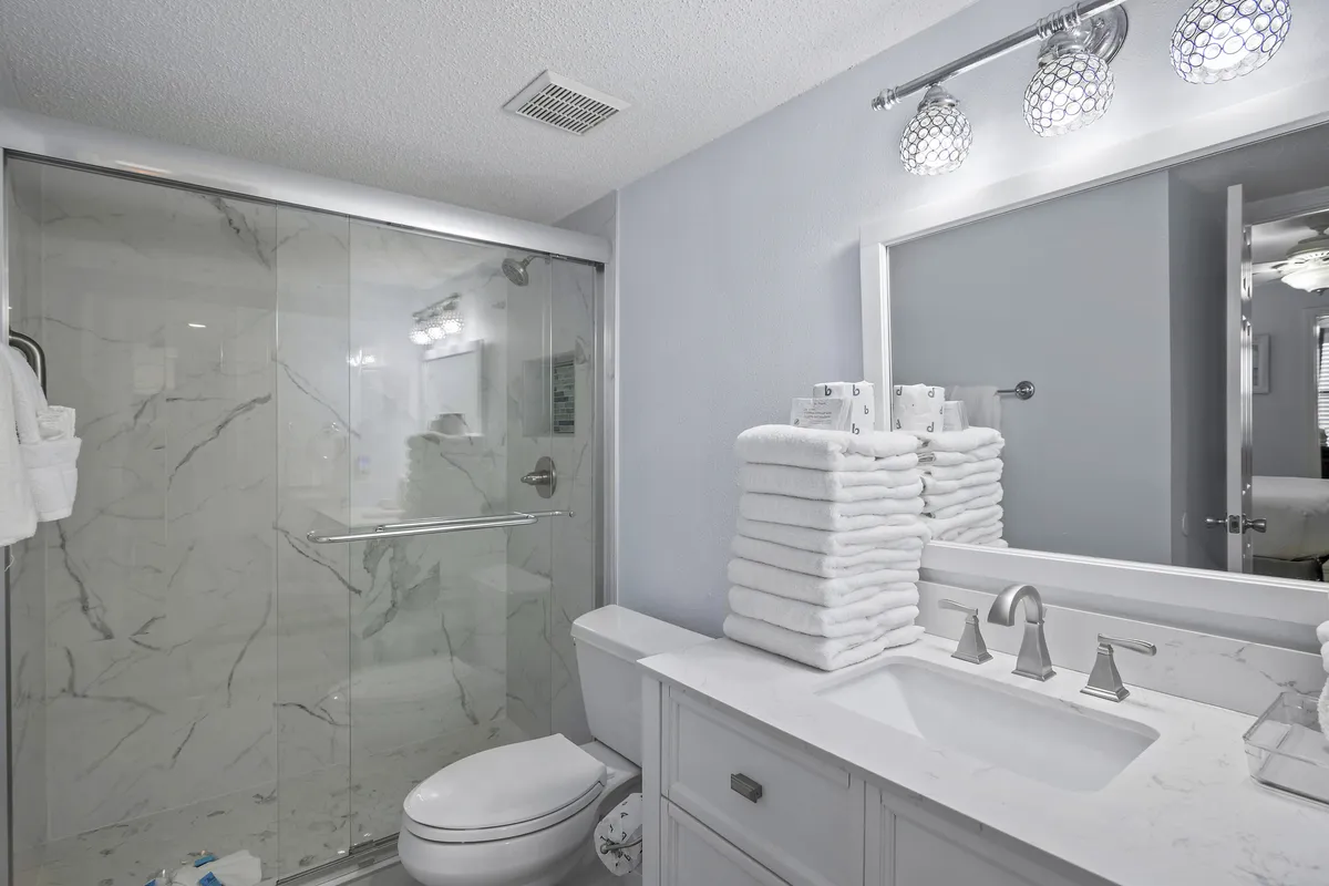A modern bathroom with a glass-enclosed shower, stacked fluffy white towels, a sleek vanity with sink, and soft lighting. Everything is neat and spa-like, suggesting a refreshing place to unwind.